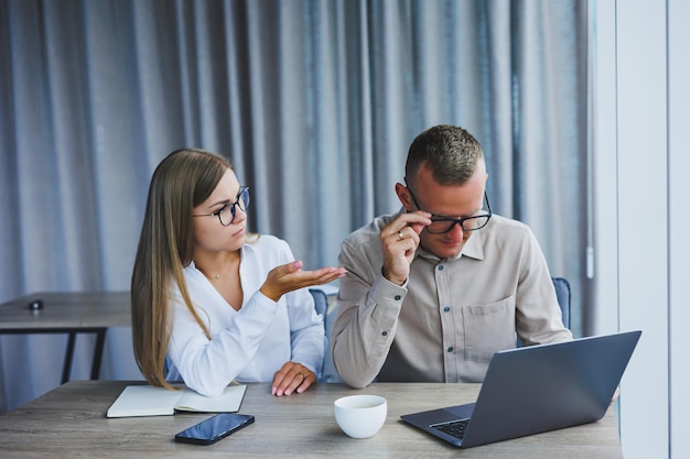 Los hombres de negocios están discutiendo mientras trabajan con una computadora portátil en la oficina Gente de negocios enfocada que coopera en un espacio de trabajo moderno Dos jóvenes hombres de negocios están sentados juntos en una mesa