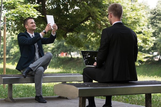 Hombres de negocios felices usando Tablet Pc afuera en un banco del parque