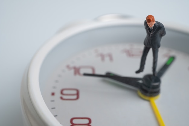 Los hombres de negocios de la figura miran y piensan y están parados en la esfera blanca del reloj junto a la esfera del reloj que muestra la hora.