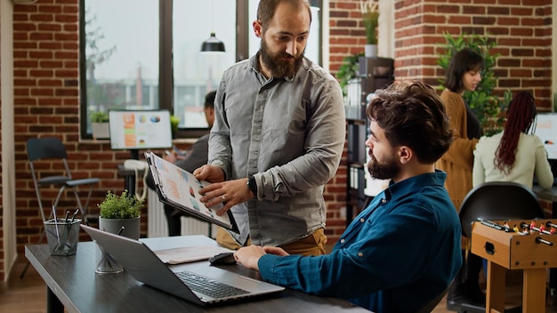 Hombres de negocios intercambian ideas para planificar informes de datos en línea en una computadora portátil, trabajando con información corporativa para hacer un proyecto de investigación. Usar cuadros y gráficos para hacer presentaciones con un colega.