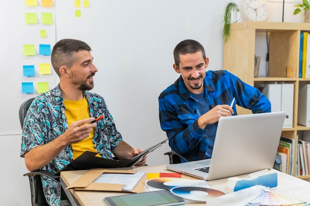 Hombres de negocios jóvenes felices en la oficina de inicio trabajando en equipos portátiles Hombres de negocios con pegatinas post-it