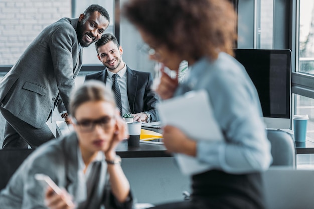 hombres de negocios multiétnicos sonrientes mirando a mujeres de negocios en la oficina