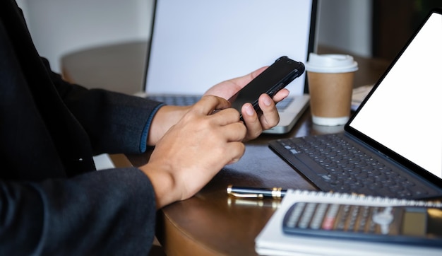 Hombres de negocios que trabajan en una computadora portátil y sostienen un teléfono inteligente con una taza de café en la mesa en una cafetería o café que trabaja desde el concepto de trabajo independiente de café