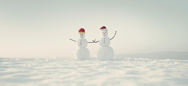 Hombres de nieve de nieve en santa sombrero pareja de muñeco de nieve al aire libre felices fiestas y celebración