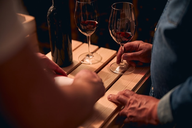 Hombres no reconocidos de pie cerca de la caja de madera con vasos de vino tinto