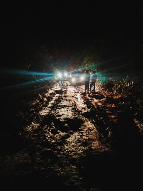 Foto hombres de pie junto a un coche iluminado en un camino de tierra