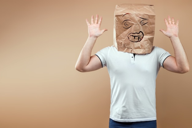 Los hombres se ponen una bolsa de papel con una cara de miedo pintada en la cabeza, levantan las manos, se rinden. Aislar sobre un fondo amarillo, las imágenes son fáciles de recortar para usar en cualquier lugar, copie el espacio.