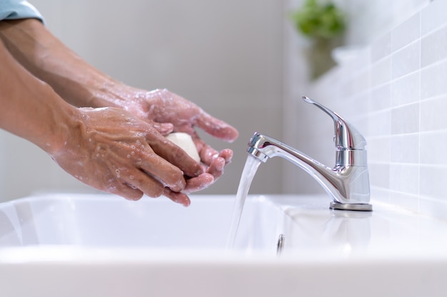 Hombres que se lavan las manos con jabón y agua limpia frente al lavabo del baño para evitar la propagación de gérmenes. Lavarse las manos con jabón.