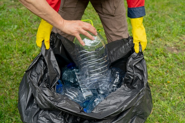 Hombres recogiendo basura. Mano poniendo una botella de plástico en una bolsa de basura de plástico.