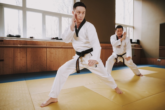 Hombres en ropa blanca y cinturones negros entrenan.