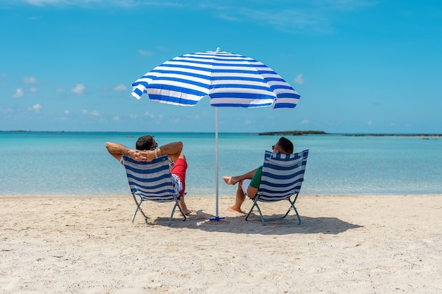 Hombres sentados en sillas bajo una sombrilla en una playa tropical