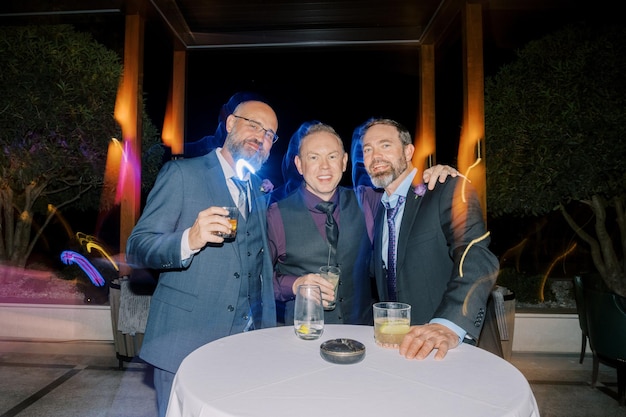 Hombres sonrientes con vasos de whisky de pie en la mesa