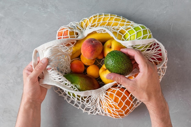Los hombres toman a mano aguacate de bolsas de compras de malla con productos de frutas orgánicas Comprador de malla ecológico Concepto libre de plástico