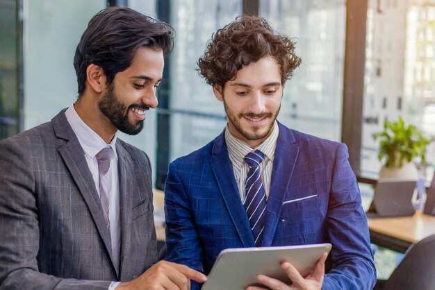 Hombres de trabajo en equipo reunión moderna con dos hombres de negocios con tableta en el trabajo de interiores de la oficina