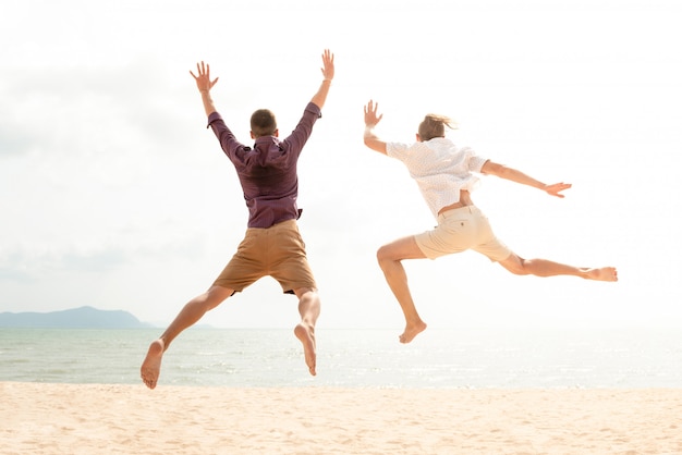 Hombres turísticos felices enérgicos jovenes que saltan en la playa