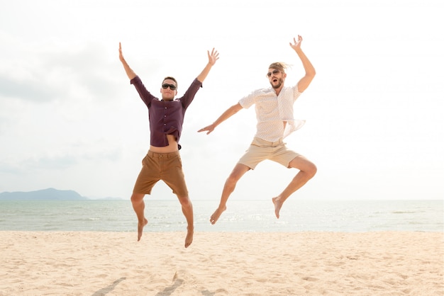 Hombres turísticos felices enérgicos jovenes que saltan en la playa