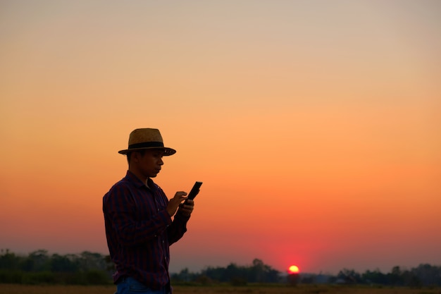 Hombres vestidos con camisas a rayas con un sombrero de paja para usar el teléfono al atardecer con espacio de copia