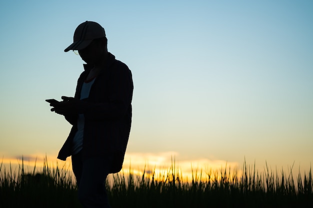 Foto hombres vestidos con camisas a rayas con un soporte de gorra para usar el teléfono al atardecer con espacio de copia. silueta de un hombre con un sombrero usando un teléfono.