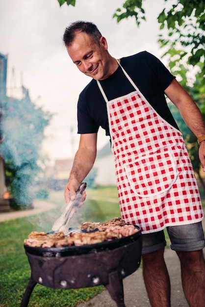 Foto hombres vestidos con delantal asando carne en el patio trasero