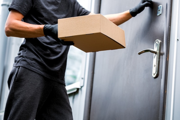 Home Delivery Shopping Box Mann mit Handschuhen und Schutzmaske liefert Pakete an der Tür.