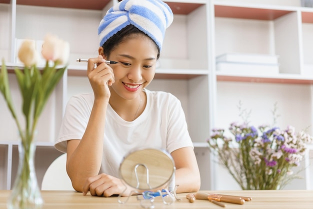 Home Lifestyle-Konzept Junge Frau in Turban nach der Dusche und Eyeliner auf Augenlid für Make-up auftragen