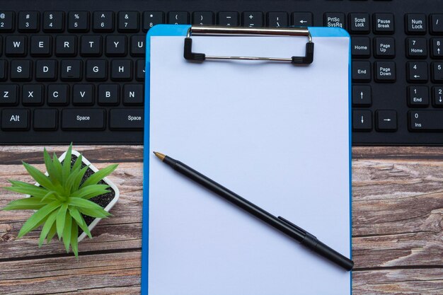 Foto home-office-arbeitsplatz mit schwarzer tastatur, blauer zwischenablage, stift und topfpflanze. flache lage, ansicht von oben