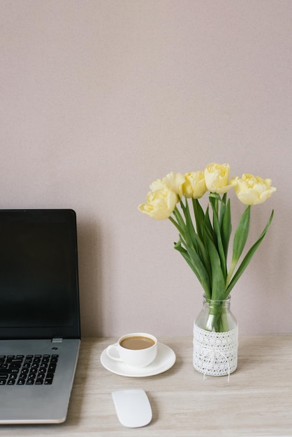 Home Office Interior Ein Laptop ein Strauß gelber Tulpen in einer Vase eine Tasse Kaffee Mittagspause