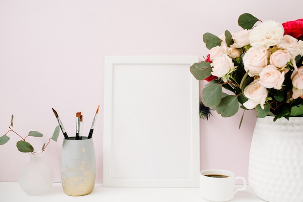 Home-Office-Schreibtisch mit Fotorahmenmodell, schönen Rosen und Eukalyptus-Bouquet