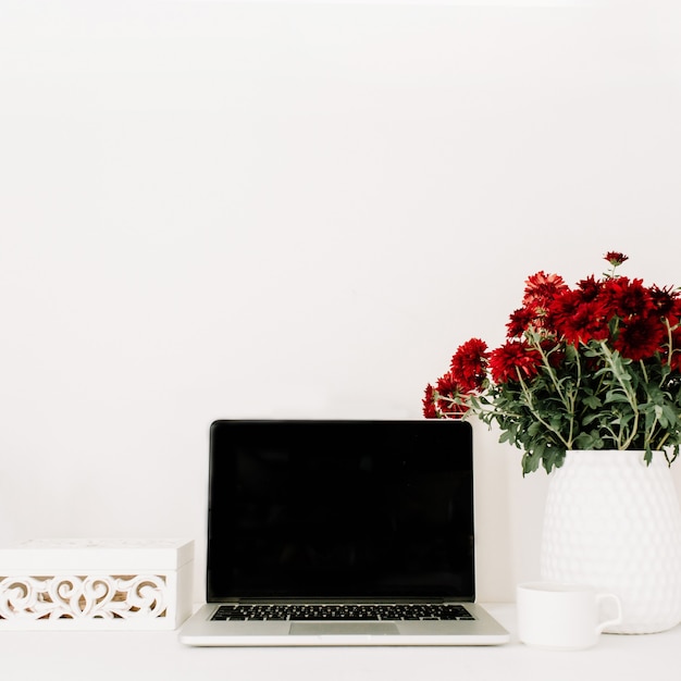 Home-Office-Schreibtisch mit Laptop, schöner roter Blumenstrauß, weiße Vintage-Schatulle vor weißem Hintergrund