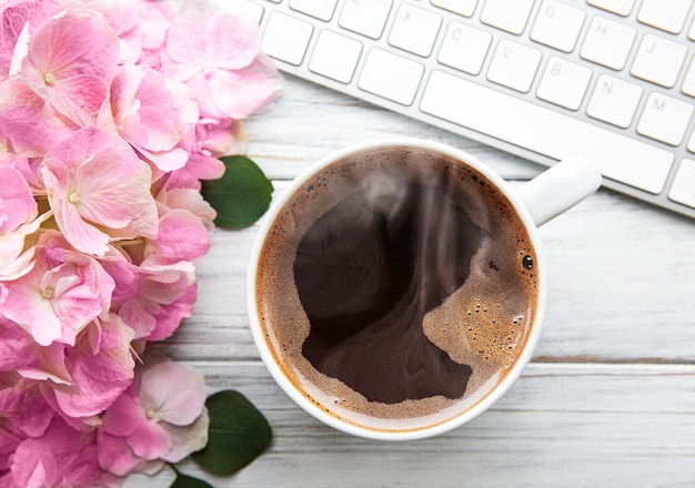 Home-Office-Schreibtisch mit rosa Hortensien-Blumenstrauß, Tasse Kaffee und Tastatur