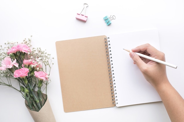 Home-Office-Schreibtisch Tisch mit Frauenhand, Notizblock, Blume auf weißem Hintergrund.