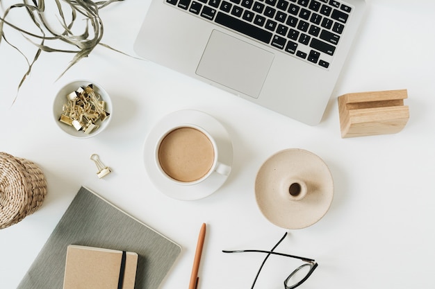 Home-Office-Schreibtischarbeitsbereich mit Laptop, Kaffeetasse, Notizbuch, Brille, Stift, grünem Pflanzenzweig auf weißer Oberfläche