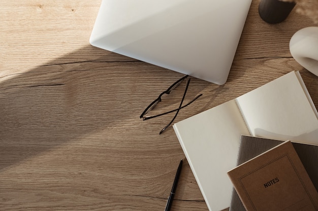 Home-Office-Schreibtischarbeitsplatz mit Laptop, Notebook, Brille, Sonnenlichtschatten