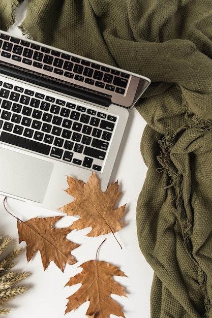 Home Office Tisch Schreibtisch Arbeitsbereich mit Laptop, trockenem Herbstlaub und Decke. Flache Lage, Draufsicht.