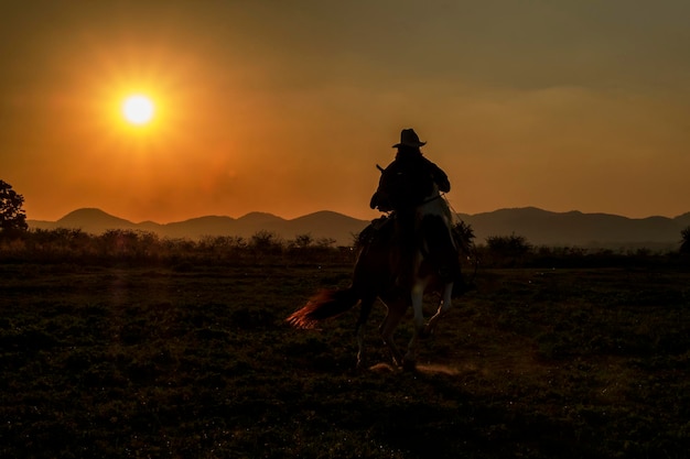 Foto homem a cavalo no campo durante o pôr-do-sol