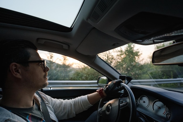 Foto homem a conduzir um carro de luxo ao pôr-do-sol