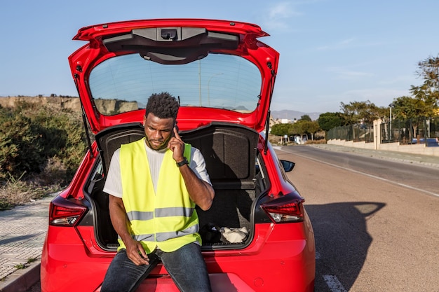 Homem a falar ao telemóvel na parte de trás do seu carro vermelho