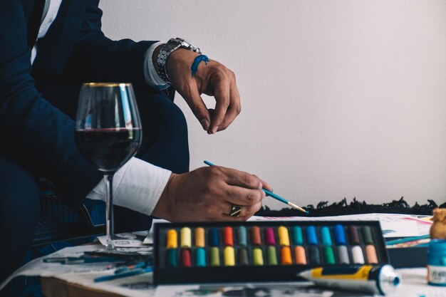 Foto homem a pintar com uma chávena de vinho na mesa