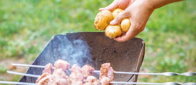 Homem a preparar carne de churrasco com batatas