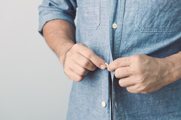 Homem abotoando a camisa jeans azul Studio filmado no fundo da parede cinza