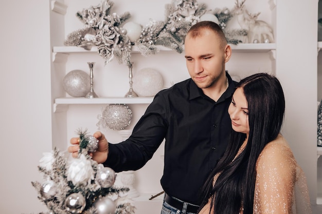 Homem abraça uma mulher com barriga redonda com bebê dentro de decorar a árvore de Natal, comemorando o Ano Novo