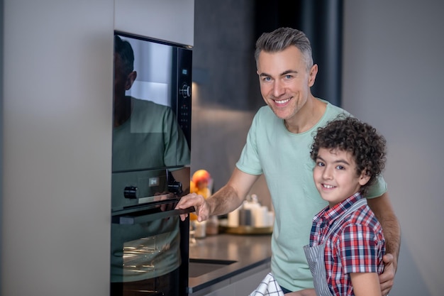 Homem abraçando filho sorrindo para a câmera perto do forno