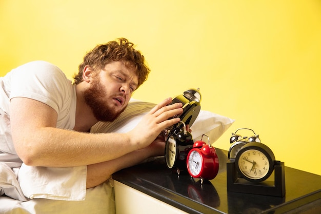 Homem acorda e ele está bravo com o relógio tocando, tentando desligá-lo, parece sonolento