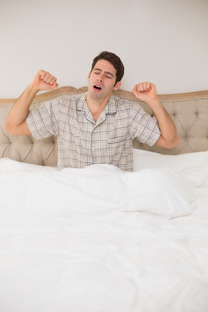 Homem acordado na cama e esticando os braços