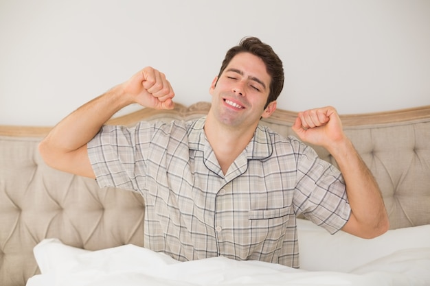 Foto homem acordado na cama e esticando os braços