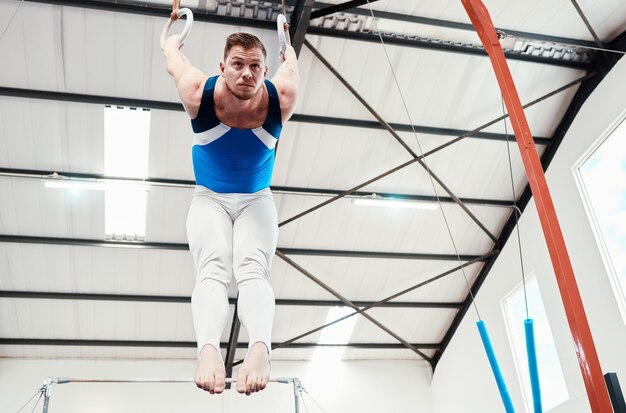 Foto homem acrobata e equilíbrio de ginástica em anéis em fitness para treinamento prático ou treino na academia ginasta profissional pendurado em círculos de anel para acrobacias atléticas ou exercícios de força
