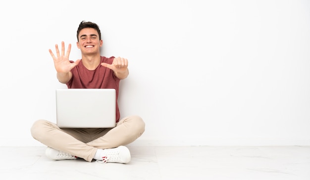 Homem adolescente sentado na flor com seu laptop contando seis com os dedos