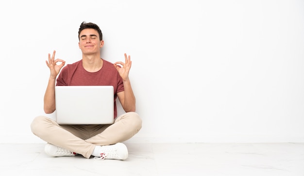 Homem adolescente sentado na flor com seu laptop em pose de zen