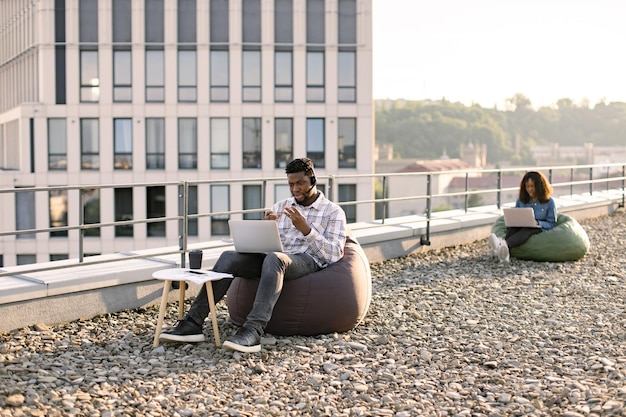 Homem adulto africano usando fone de ouvido realizando conferência através de computador portátil