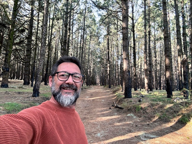 Homem adulto alegre feliz tirando uma foto selfie na floresta desfrutando de atividades de lazer ao ar livre no parque florestal nacional sozinho Aventura e estilo de vida pessoas árvores altas em fundo Sustentabilidade